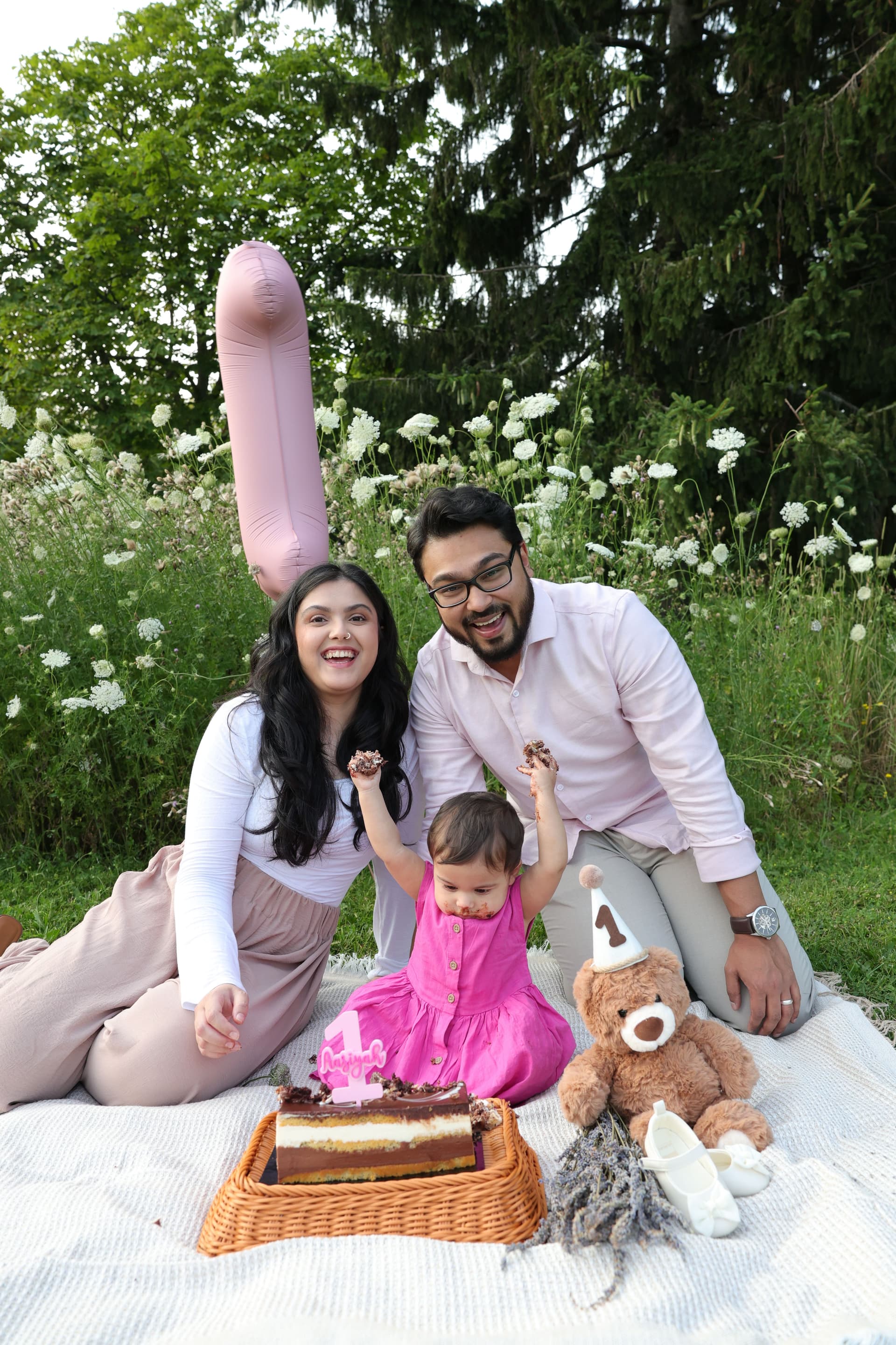 Family laughing together during an outdoor first-birthday cake celebration
