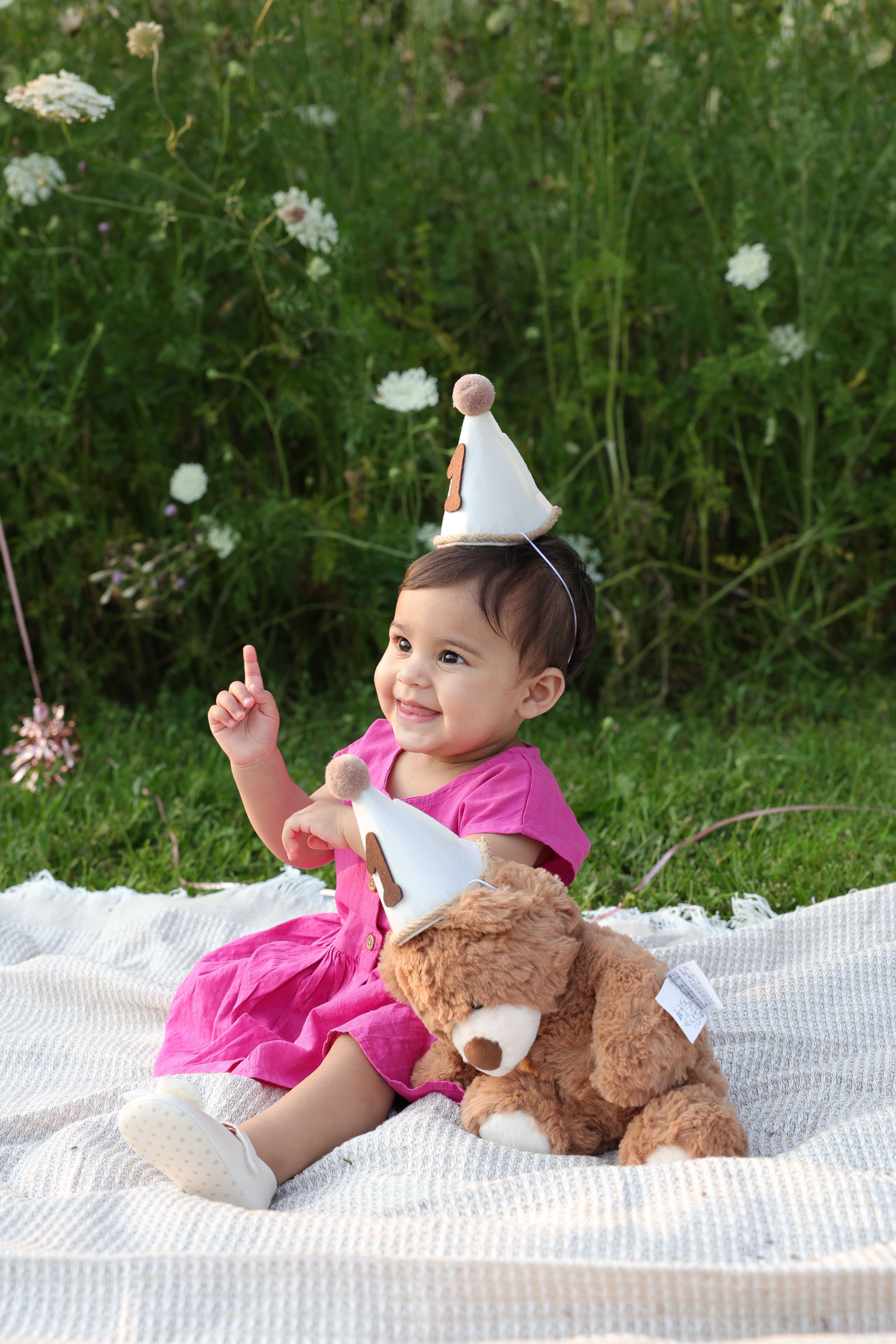 One-year-old sitting with a teddy bear and matching first-birthday party hats